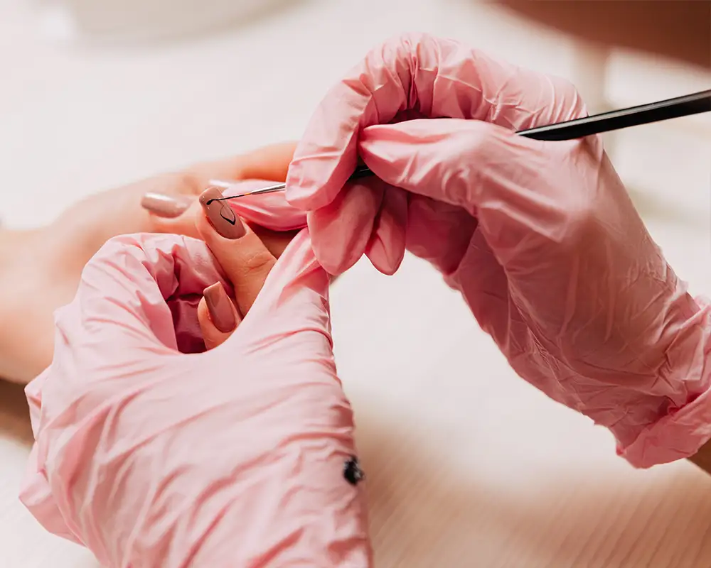 Ablauf einer Maniküre. Eine professionelle Maniküristin zeichnet mit schwarzem Nagellack und einem dünnen Pinsel ein Muster auf künstliche Nägel.